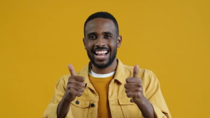 激动的非洲裔美国人肖像在黄色背景上显示竖起大拇指的手势