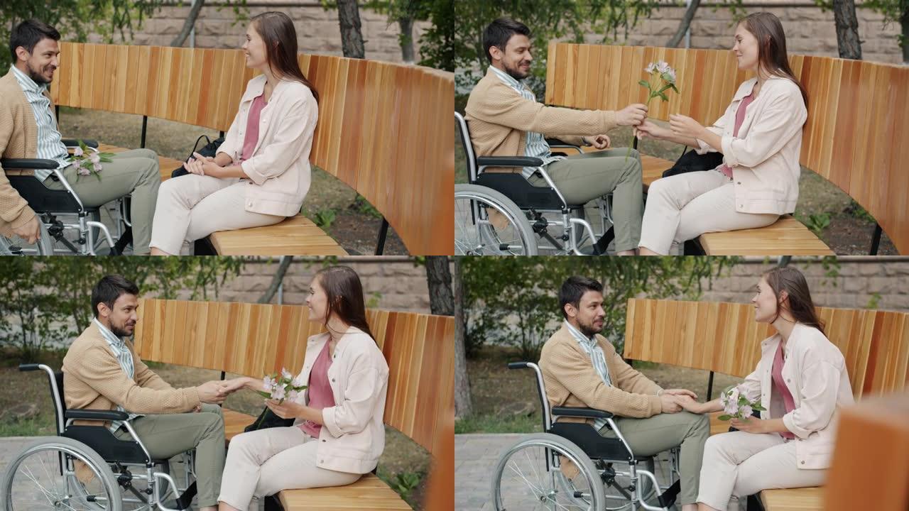坐在轮椅上的快乐男人在公园户外会见女朋友，带着鲜花谈论享受约会