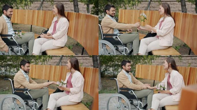 坐在轮椅上的快乐男人在公园户外会见女朋友，带着鲜花谈论享受约会