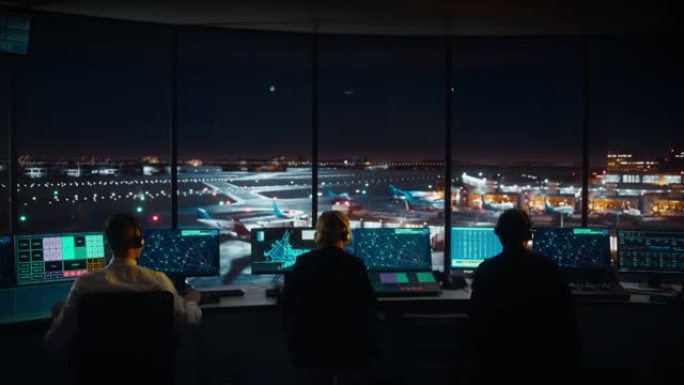 夜间在现代机场塔中工作的多元化空中交通管制团队。办公室里满是台式电脑显示屏，配有导航屏幕，飞机飞行雷