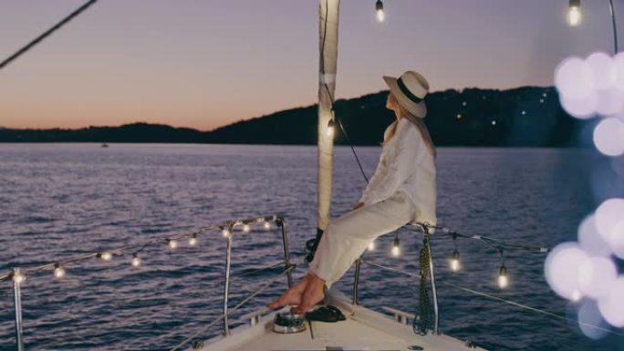 SLO MO时髦的女人从用灯串照明的帆船甲板上欣赏风景