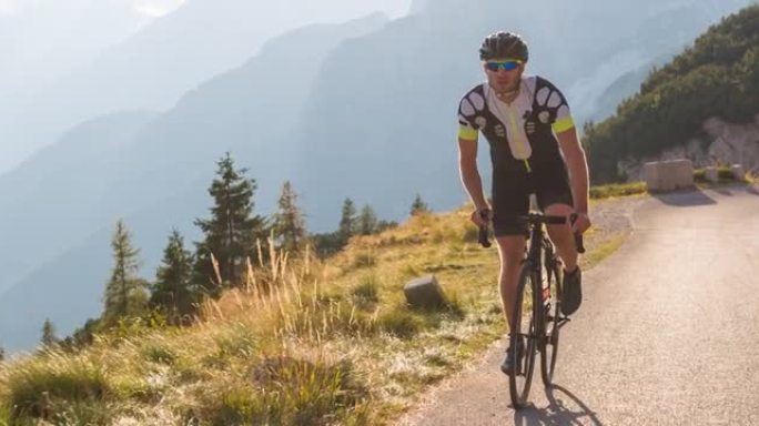 专注的年轻男运动员公路骑行上坡，踩踏板站立，背景群山