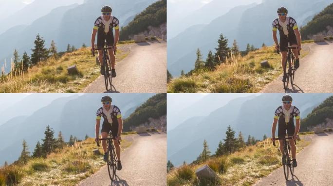 专注的年轻男运动员公路骑行上坡，踩踏板站立，背景群山