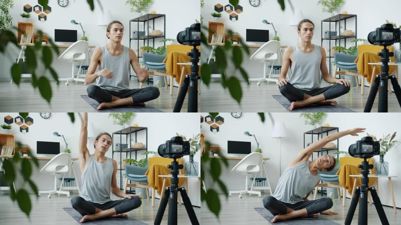 男性瑜伽老师vlogger在现代公寓中使用相机录制教程坐在垫子上聊天