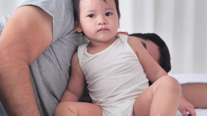 疲惫的千禧一代亚洲父亲睡在床上，想让宝宝儿子睡觉，活跃的宝宝玩一整天。