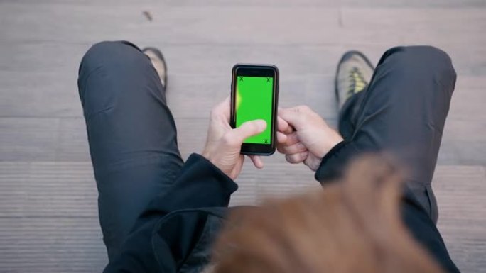 坐在台阶上时，无法识别的男子使用带有绿屏的智能手机