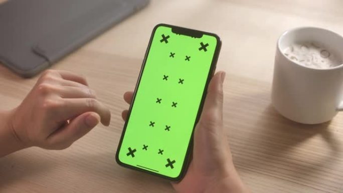在家里的办公桌上使用带有绿屏的智能手机的特写手