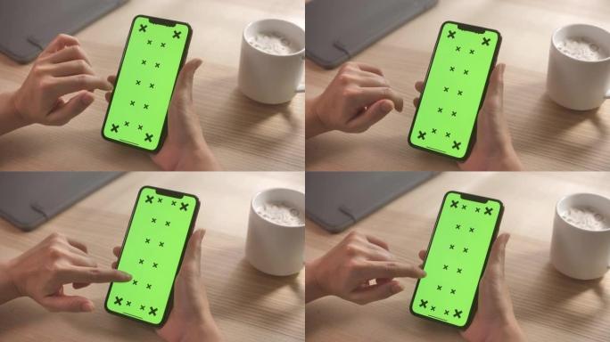 在家里的办公桌上使用带有绿屏的智能手机的特写手