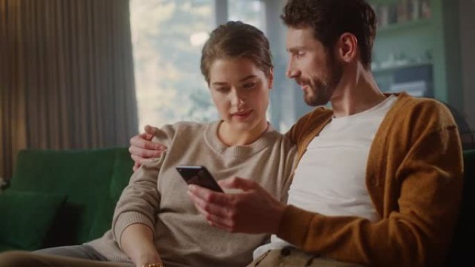 夫妇坐在舒适公寓的沙发上时，使用智能手机设备。男女朋友聊天，在互联网上进行电子购物，观看有趣的视频，