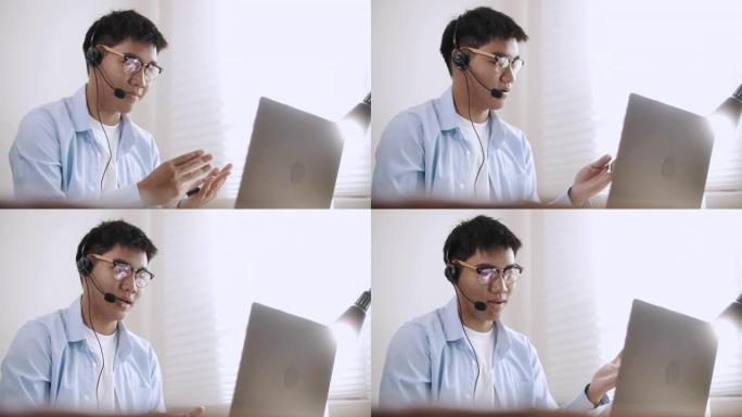 亚洲商人戴着耳机在笔记本电脑上进行会议视频通话