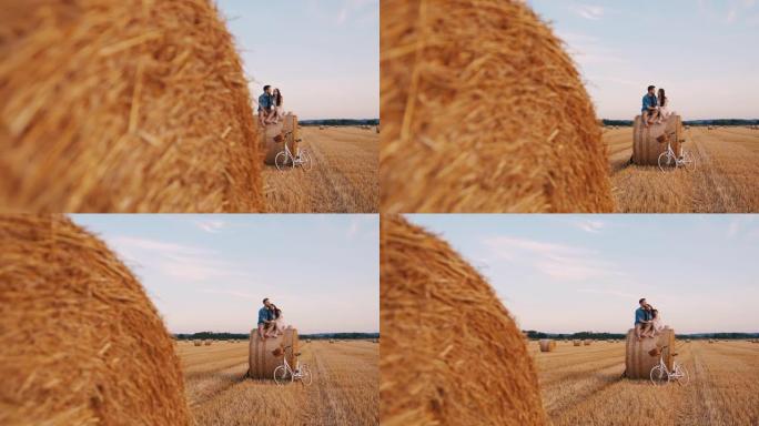 手持慢动作镜头的成年夫妇坐在田野里的干草捆上，拥抱并欣赏日落