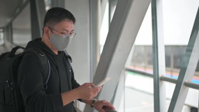 一名戴着防护口罩的亚洲华人男子行走在城市桥梁上，用智能手机手机应用查看金融股市场分析，受新冠肺炎疫情