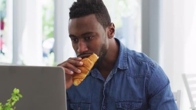 非裔美国商人使用笔记本电脑并在咖啡馆吃羊角面包
