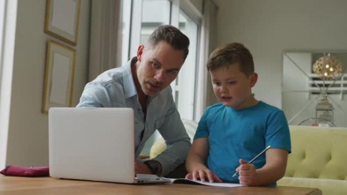 高加索父亲和儿子坐在餐桌旁，在家用笔记本电脑学习