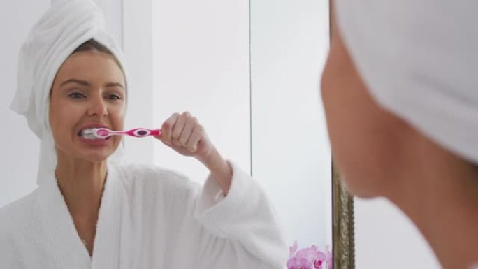 穿着浴袍的女人一边照镜子一边刷牙