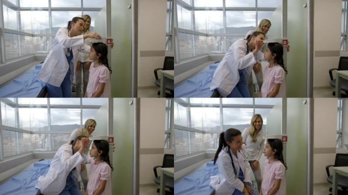 快乐的拉丁美洲儿科医生在母亲面前对一个女孩进行体检，测量她的身高