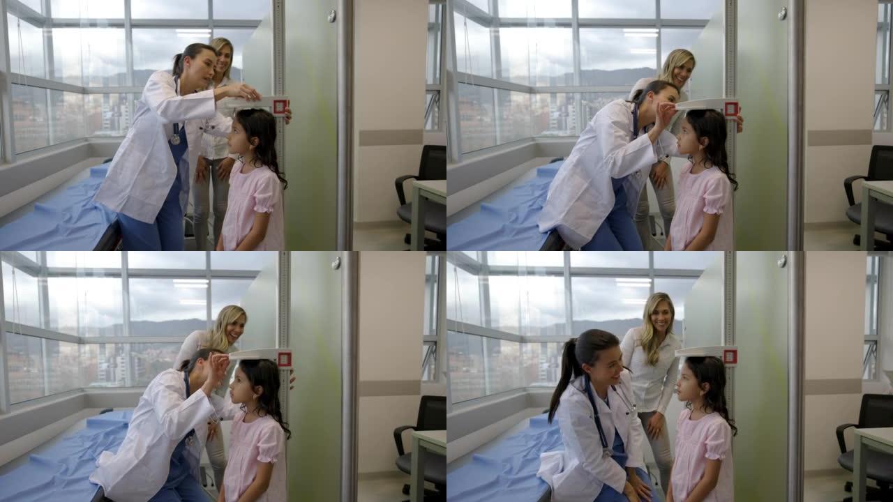 快乐的拉丁美洲儿科医生在母亲面前对一个女孩进行体检，测量她的身高