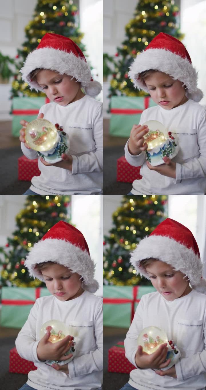 一个戴着圣诞老人帽子的高加索男孩拿着雪球的垂直镜头