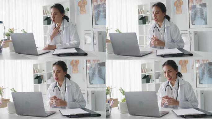 年轻的亚洲女士医生穿着白色医疗制服，配有听诊器，使用电脑笔记本电脑与患者通话视频电话。