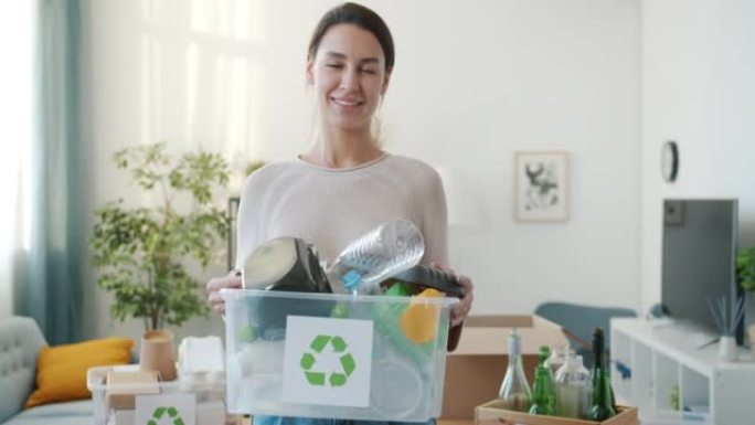 微笑的年轻女士拿着塑料回收容器站在家里