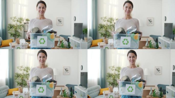 微笑的年轻女士拿着塑料回收容器站在家里