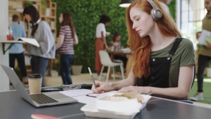 女人，笔记本电脑和笔记本电脑放在桌子上，在办公室或科技创业时听音乐。女孩，电脑和网络上的流媒体歌曲或