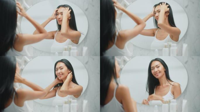 美丽的亚洲女人扮演并欣赏她郁郁葱葱的黑色长直发。年轻的成年女性在浴室镜子里享受她的自然之美。健康概念