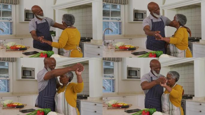 非裔美国高级夫妇穿着围裙在家里的厨房里一起跳舞
