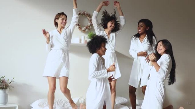 穿着白色浴袍的多样化美女在床上跳舞。