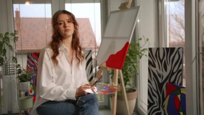一位年轻女画家的SLO MO肖像在她的工作室里摆姿势