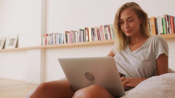 女人坐在室内的豆袋上使用笔记本电脑