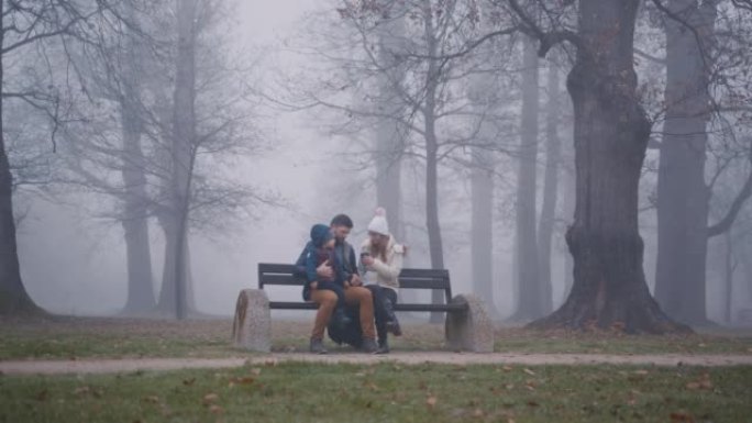 带着儿子的父母坐在公园里满是雾的长凳上