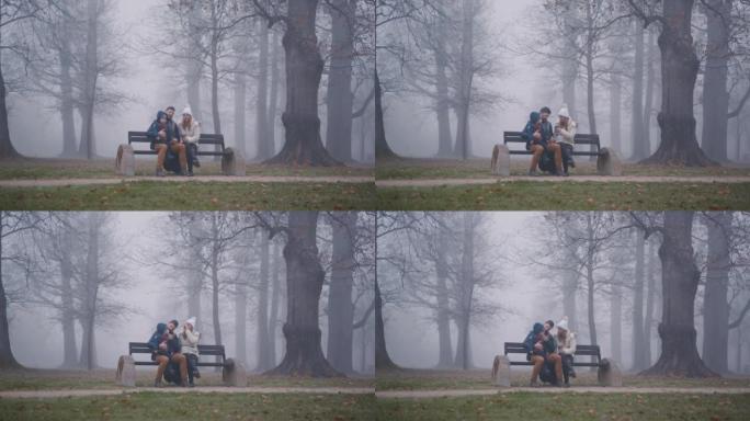 带着儿子的父母坐在公园里满是雾的长凳上