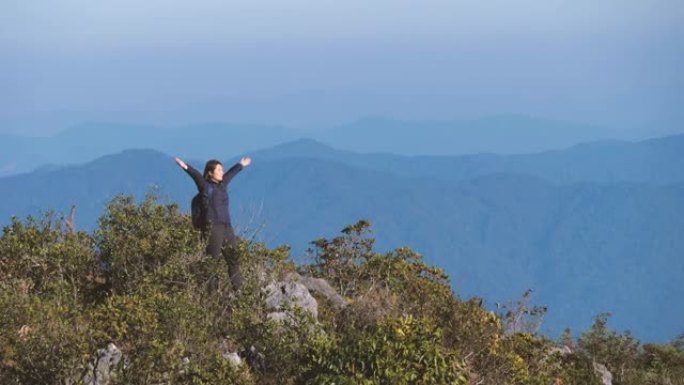 女人爬到山顶，举手庆祝成功