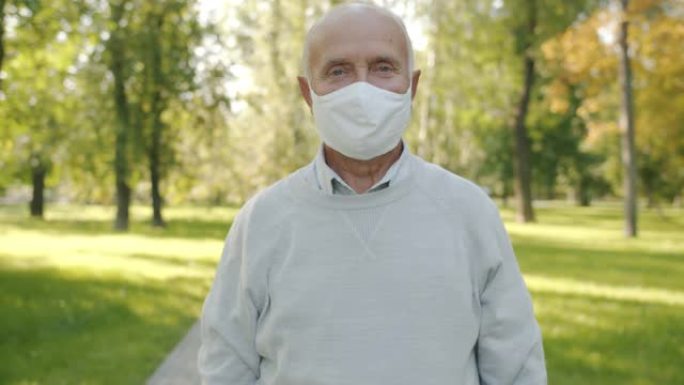 戴着医用口罩的老人的慢动作肖像独自站在夏季公园