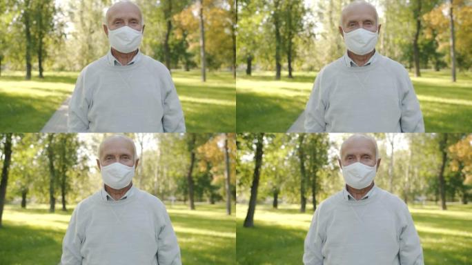 戴着医用口罩的老人的慢动作肖像独自站在夏季公园