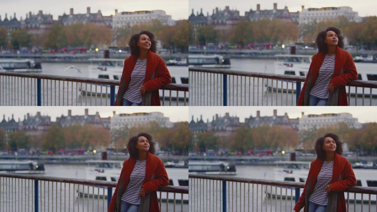 女人穿着冬衣靠在伦敦泰晤士河的栏杆上，黄昏时慢动作拍摄