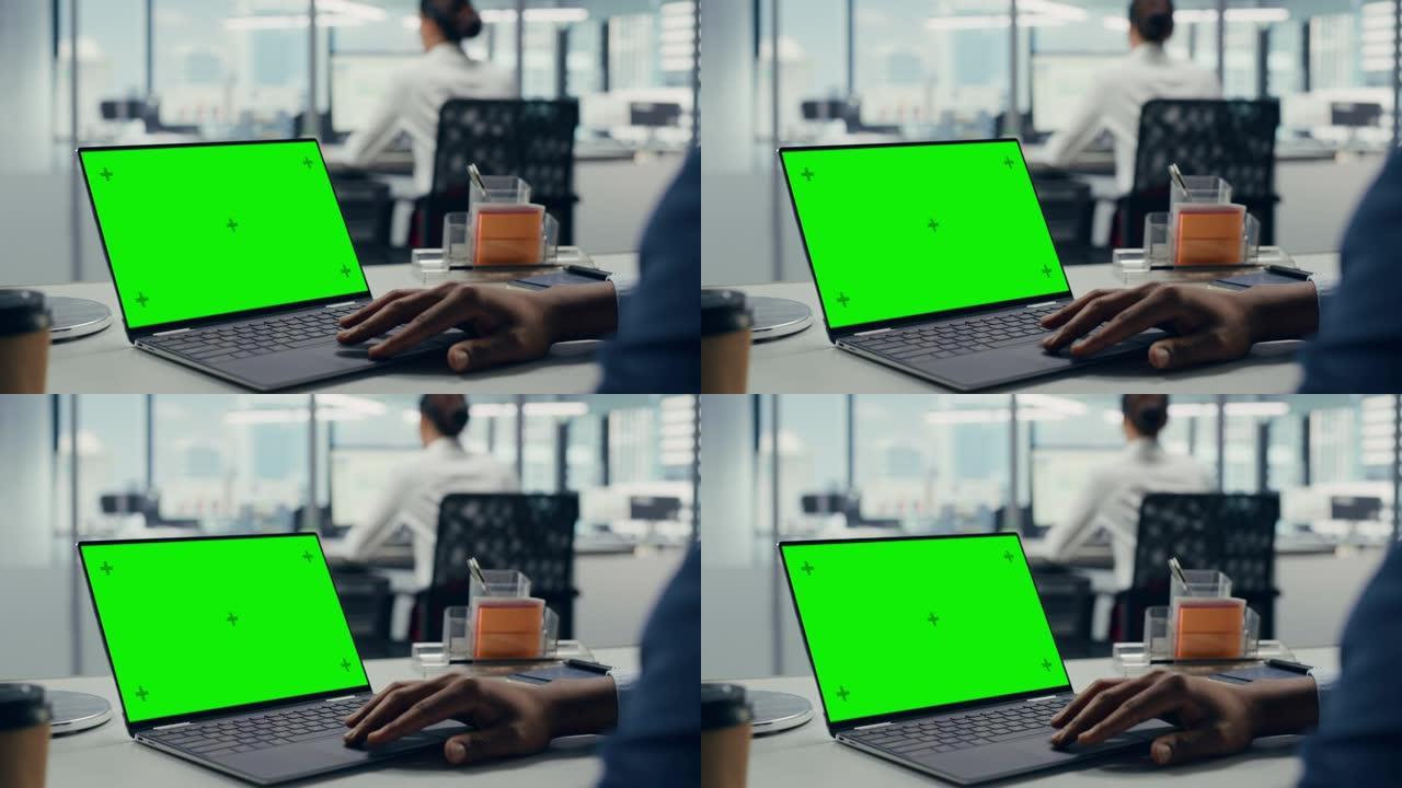 成功的黑人商人坐在办公桌前，在办公室里用绿屏笔记本电脑工作。使用色度键显示的匿名商人。时尚明亮的工作