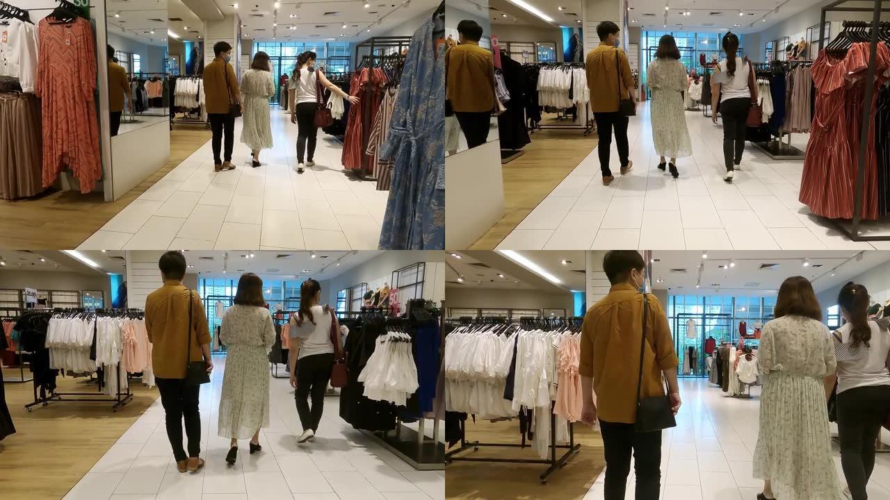 3个亚洲华裔女性朋友在服装店购物，购买带有购物袋和口罩的衣服