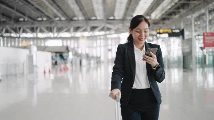 在机场使用智能手机时，女商人带着手提箱行走