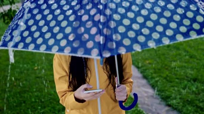 穿着雨衣的SLO MO无法识别的女人在雨中使用智能手机