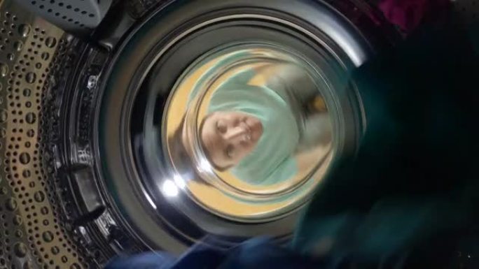 特写: 顽皮的高加索人看着一个完整洗衣机的旋转鼓。