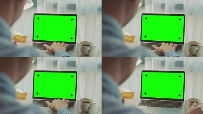 男子使用带有绿屏和手持信用卡的笔记本电脑，特写镜头