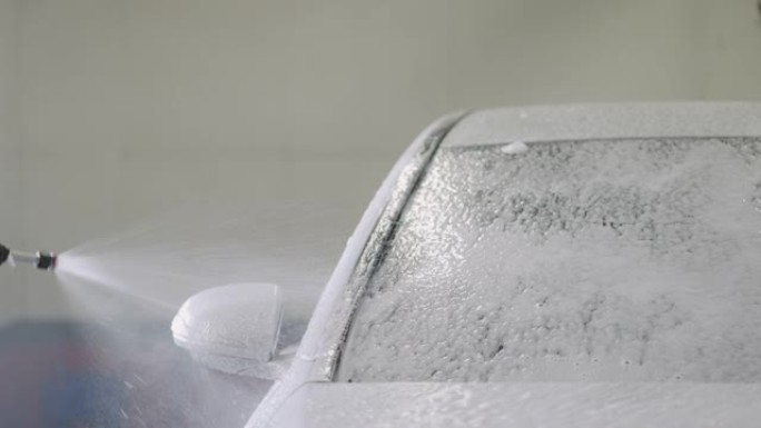 男子用喷水喷雾和肥皂泡沫清洗白色汽车