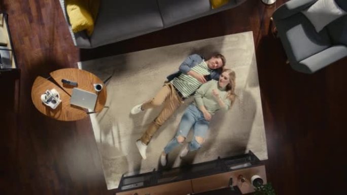 顶景公寓: 幸福的夫妇在客厅的地毯上放松，使用智能手机。女朋友和男朋友喜欢在一起，网上购物，电子商务