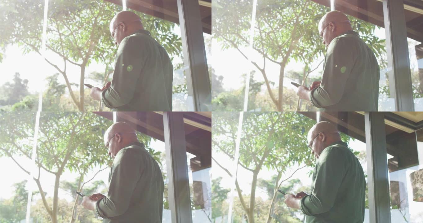 体贴的非洲裔美国老人坐在阳光下的阳台上使用智能手机