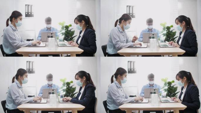 亚洲商人企业家戴着口罩，在新的正常情况下保持社交距离，以防止病毒在办公室工作时使用笔记本电脑洗手。电
