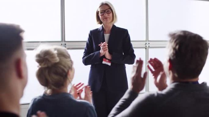 成熟的女企业家在会议上向鼓掌的同事做演讲