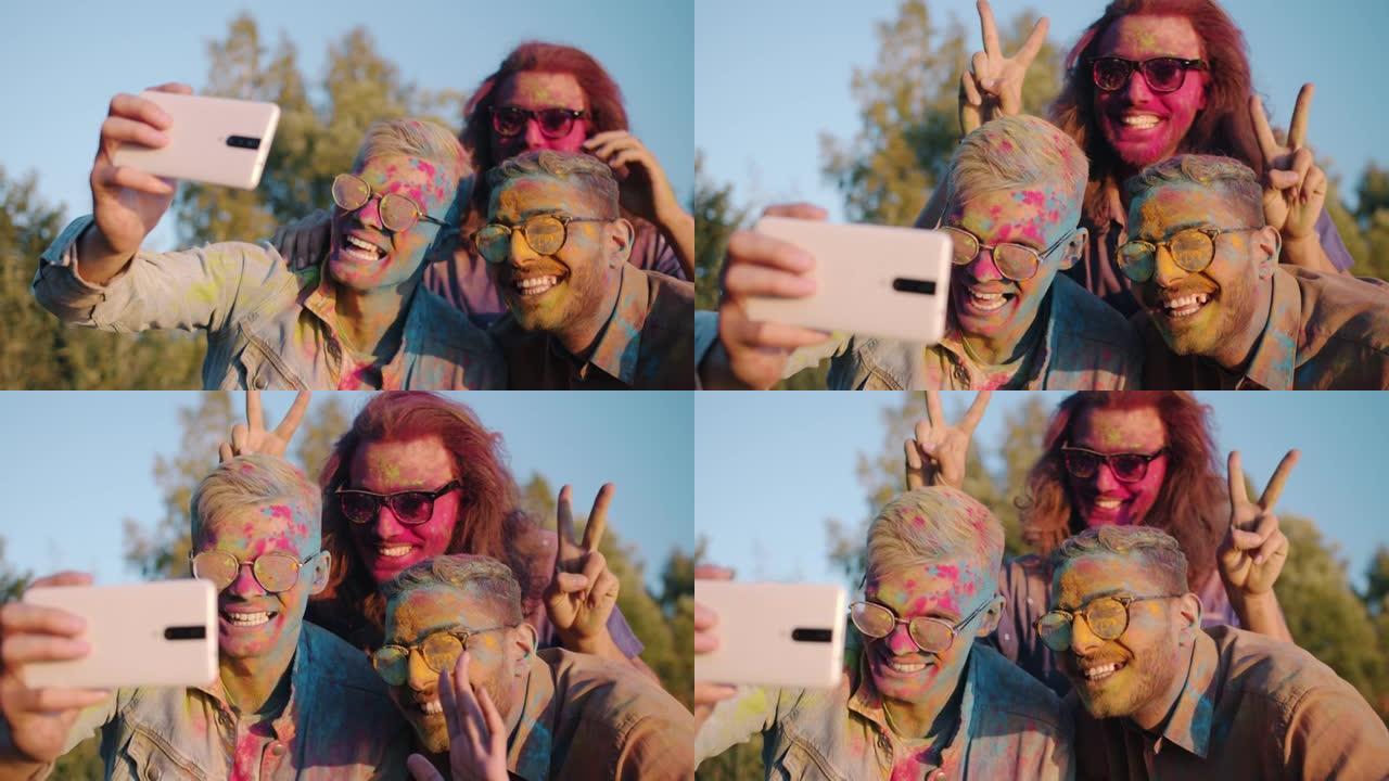 快乐的男学生享受胡里节，用智能手机摄像头自拍五颜六色的脸