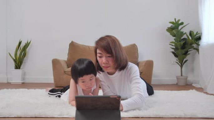 亚洲小男孩儿子5岁在家和年轻的妈妈一起学习在线课程。年轻的母亲教学校男孩帮助在家学习。呆在家里防止冠